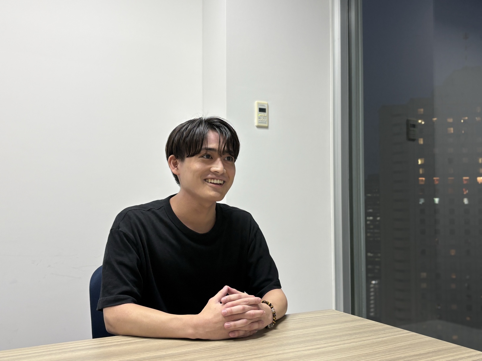 テーブルの上で手を組み、笑顔で話す飯室 歩夢